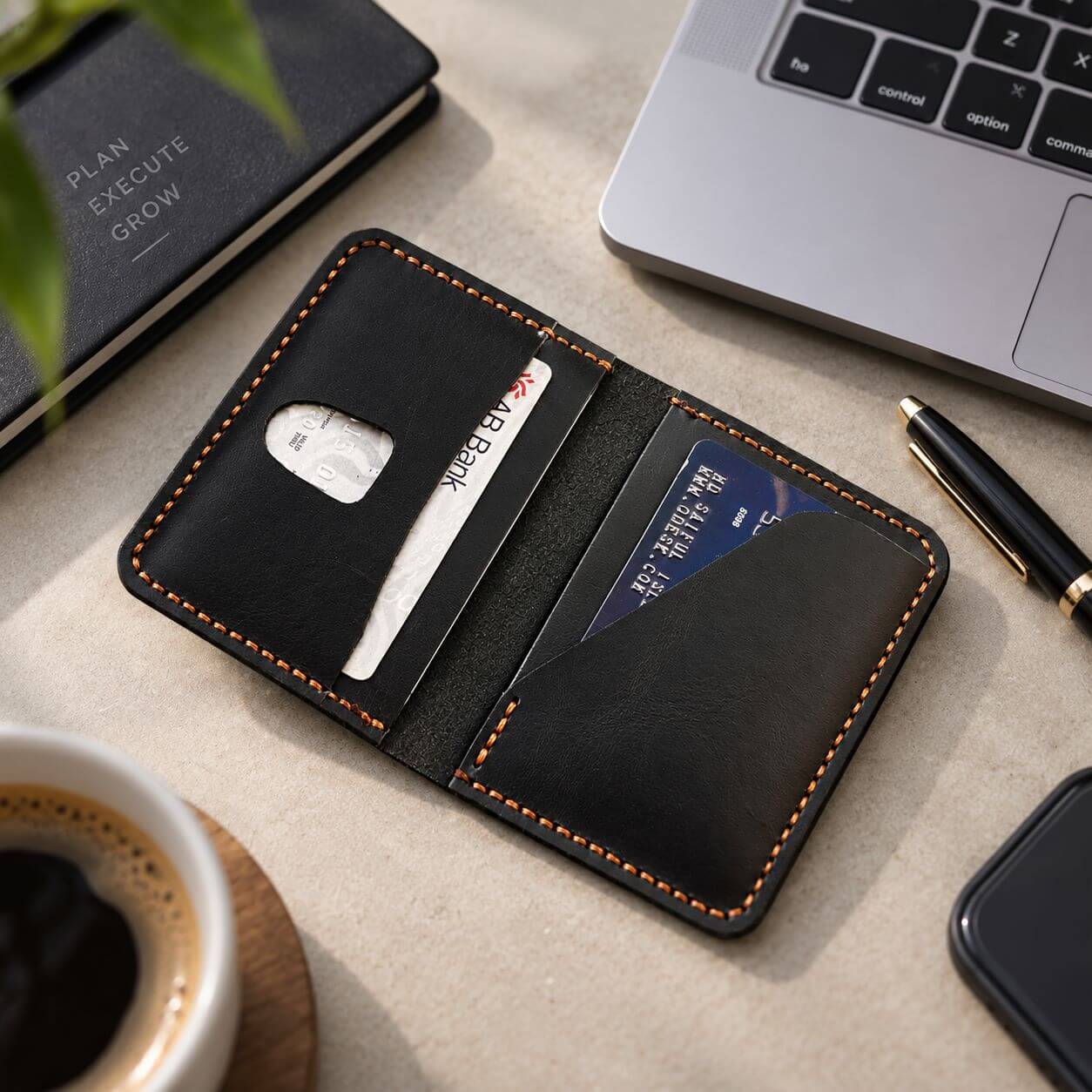 Handmade black leather card holder with orange stitching on a professional desk
