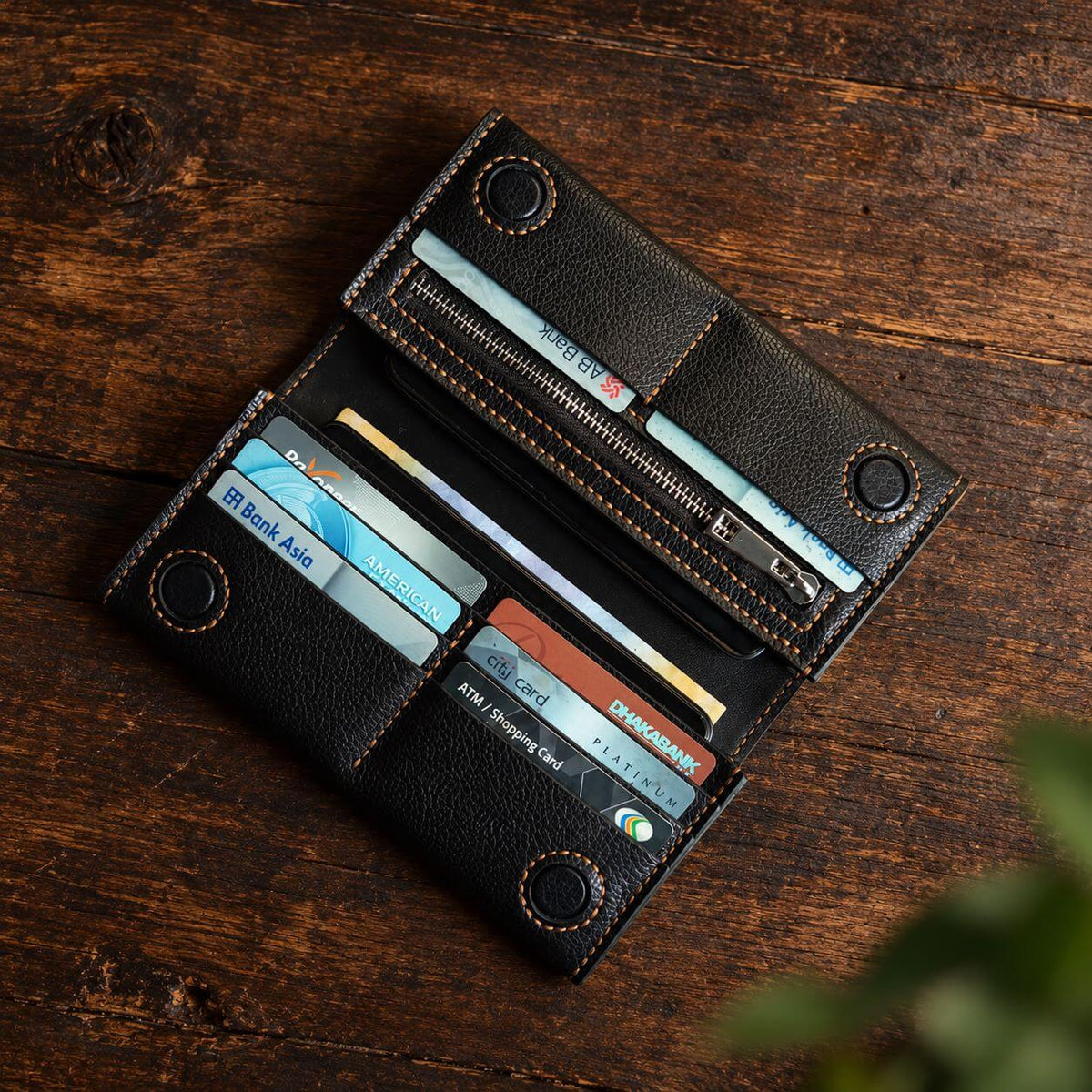 A black textured leather bi-fold wallet shown open, displaying multiple card slots, a zippered compartment, and card pockets, placed on a dark wooden surface.
